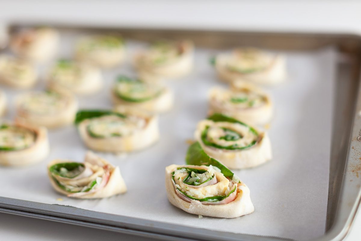 Angled view of a parchment-lined baking sheet covered with sliced tortilla pinwheels showing spirals of cream cheese, spinach and