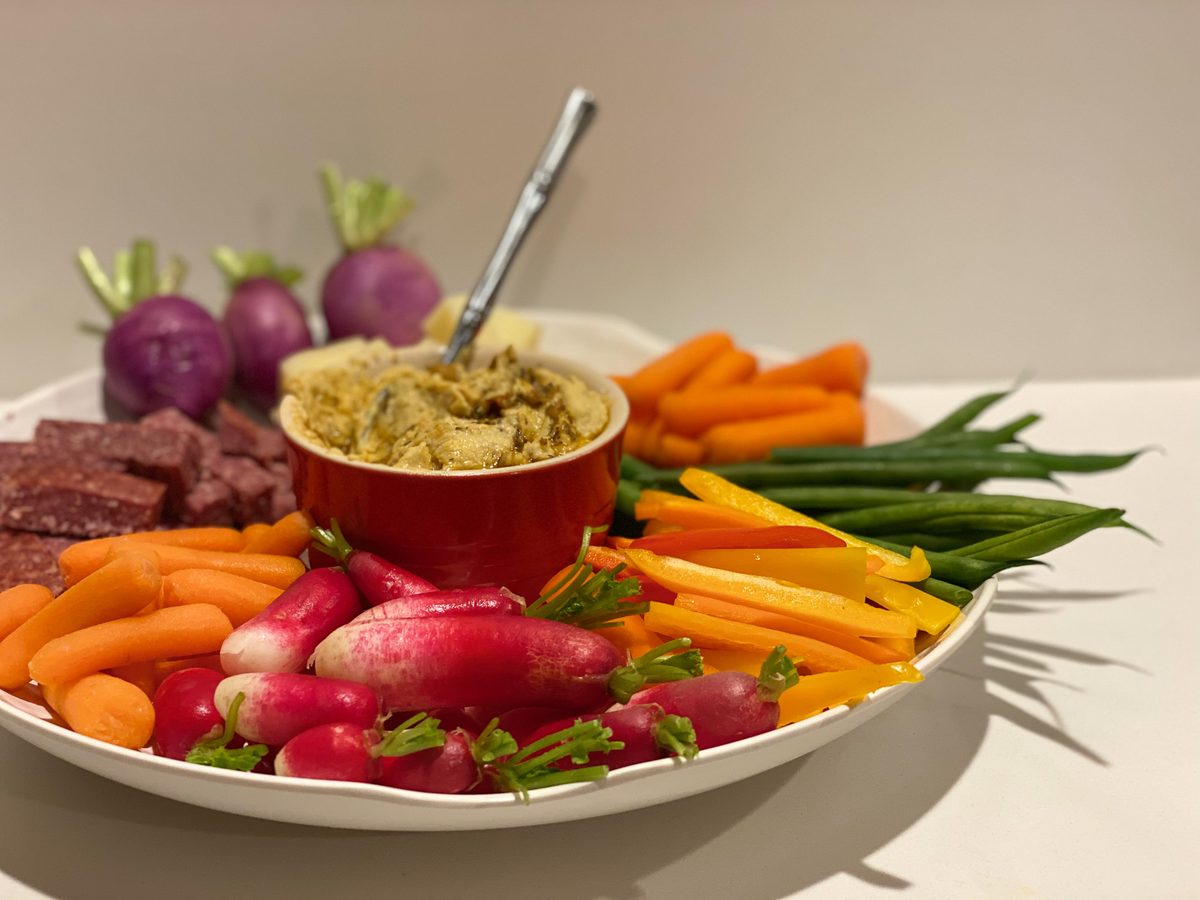 Large white platter of crudites - baby carrots, yellow pepper strips, green beans, radishes and purple-top turnips - around a red 