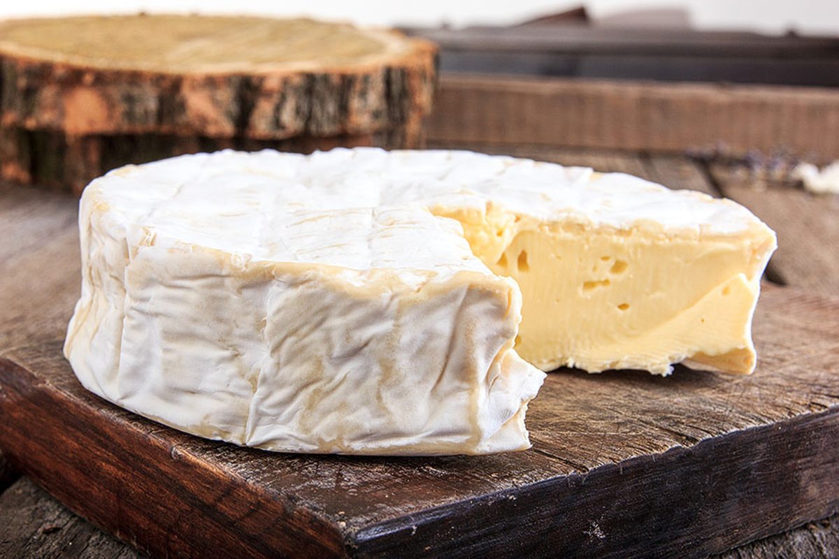 A whole white-rinded brie wheel with one wedge cut away exposing the creamy interior, sitting on a rustic dark wood board with a l
