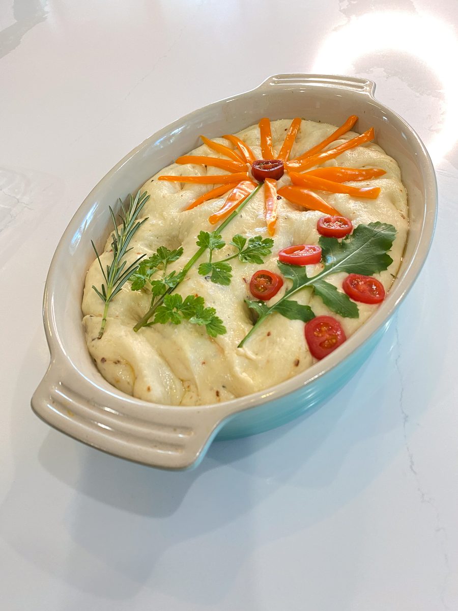 hummus in a ceramic dish decorated with carrot, tomato and herbs in a flower pattern