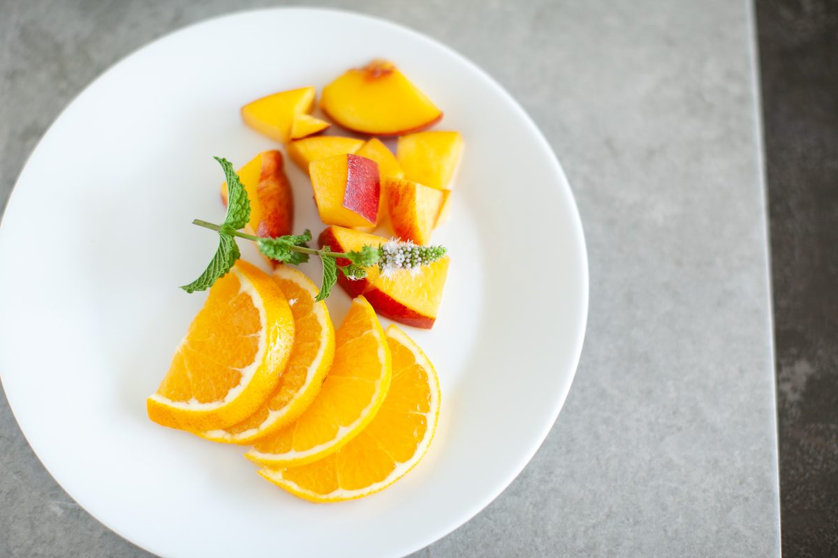 A white plate with a fanned arrangement of orange wheels and peach slices garnished with mint leaves.