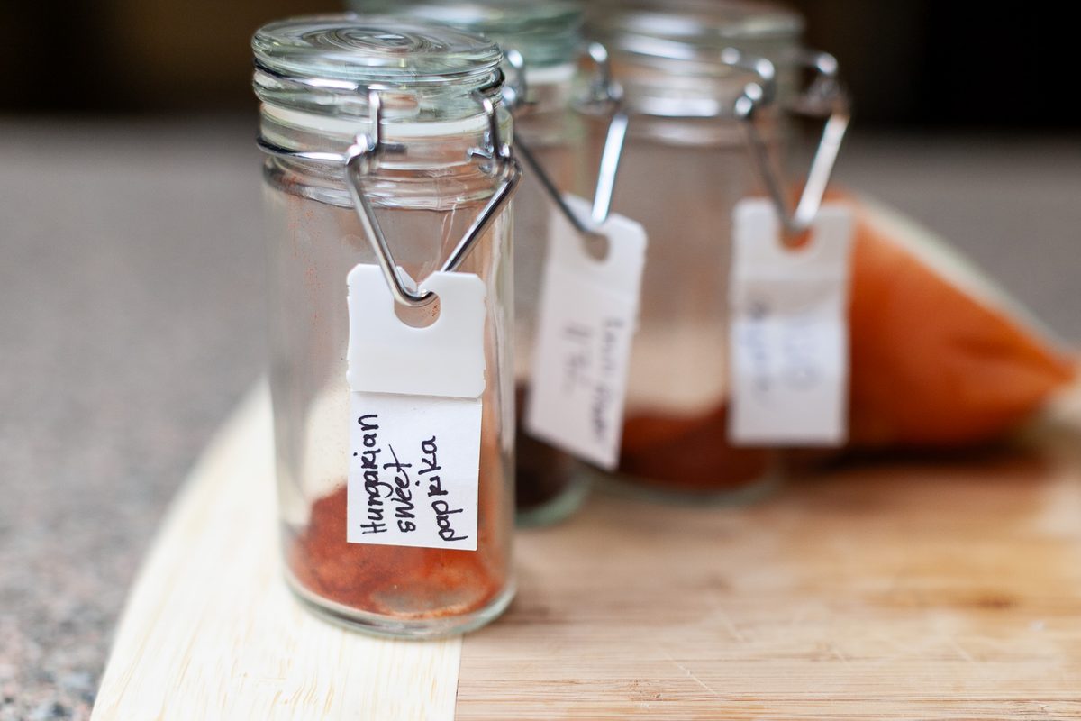 Three small clamp-lid glass spice jars with handwritten tags (the front one reads Hungarian sweet paprika) holding red ground spic