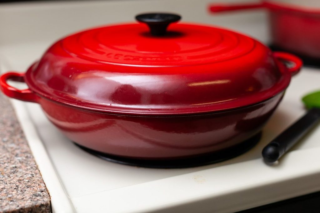 A closed red enameled cast-iron Dutch oven sitting on a white cutting board on a kitchen counter, with no food visible.