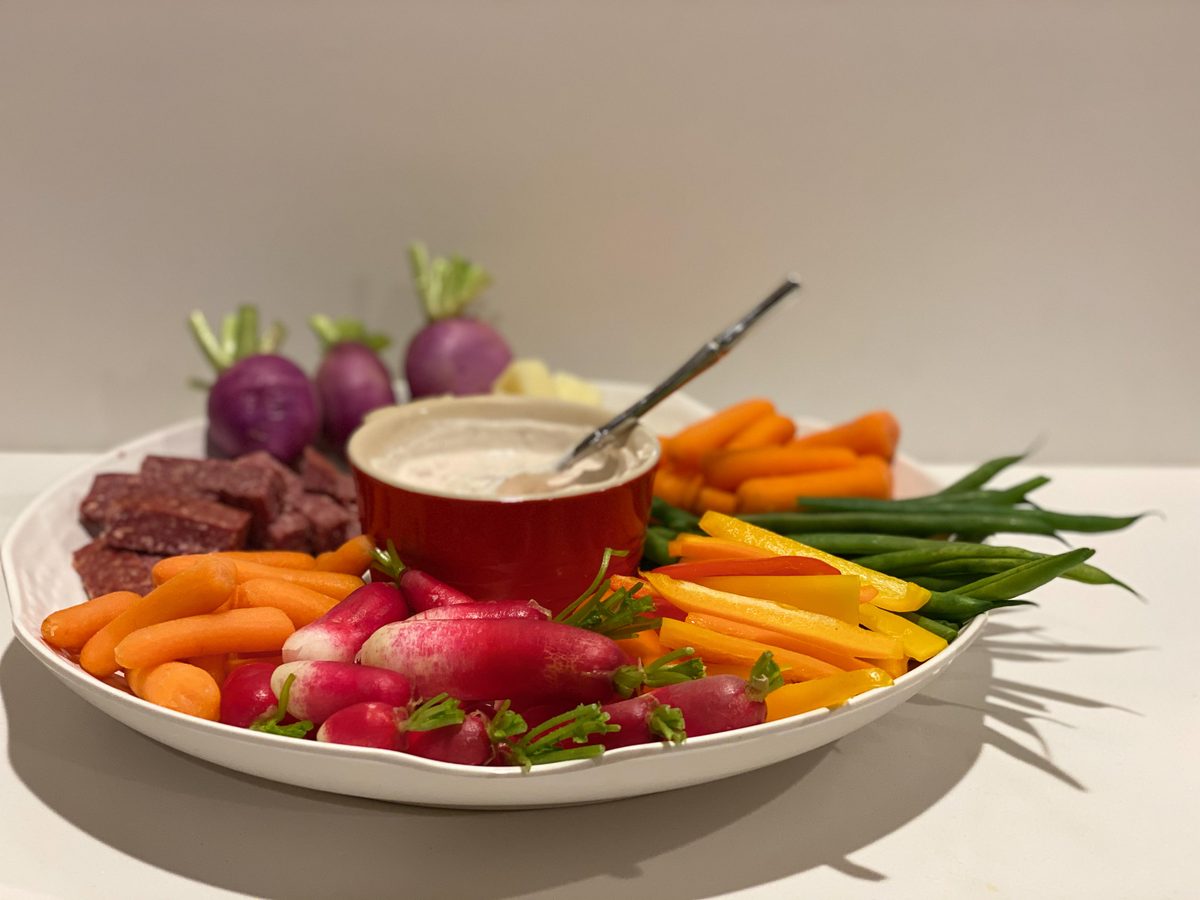 A large shallow platter of raw crudites - carrot sticks, radishes, green beans, beets and pepper strips - arranged around a small